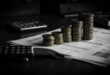 Euro coins stacked in ascending towers next to insurance documents and calculator on dark desk surface