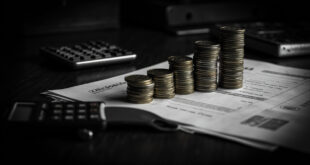 Euro coins stacked in ascending towers next to insurance documents and calculator on dark desk surface