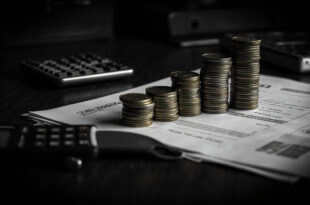 Euro coins stacked in ascending towers next to insurance documents and calculator on dark desk surface