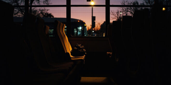Empty bus seat with small backpack in dim evening light inside parked public transit vehicle