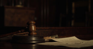 Wooden gavel resting on sound block beside scattered legal documents on polished courtroom bench