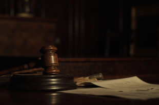 Wooden gavel resting on sound block beside scattered legal documents on polished courtroom bench