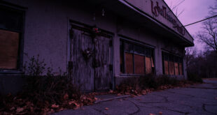 Empty shuttered building with weathered facade and scattered autumn leaves at dusk