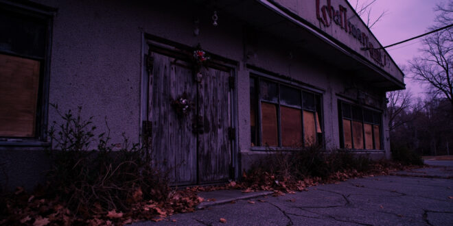 Empty shuttered building with weathered facade and scattered autumn leaves at dusk