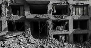 Concrete apartment building with shrapnel damage, broken windows, and large hole in upper floor surrounded by rubble