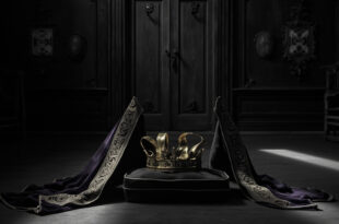 Golden ducal coronet and ceremonial Order of the Garter insignia on dark wood surface in dim historic chamber