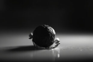 A single chocolate ball on a plain surface, wrapper partially peeled, in somber lighting