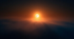 Large full moon glowing orange-amber near horizon against dark indigo night sky with atmospheric gradient