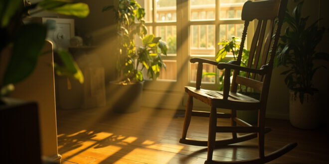 Empty wooden rocking chair next to potted plant in sunlit room with soft shadows on hardwood floor