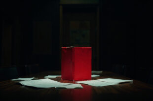 Red briefing folder on dark wooden conference table in empty meeting room with scattered papers and chairs