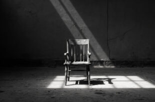 Single wooden chair alone in empty gray room with harsh shadows on bare concrete floor