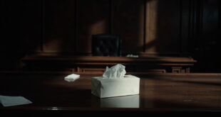 White tissue box sits on polished wooden table in empty courtroom with legal papers nearby