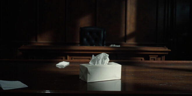 White tissue box sits on polished wooden table in empty courtroom with legal papers nearby
