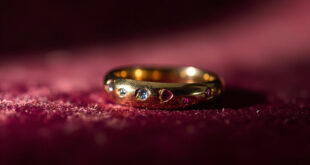 Close-up of minimalist gold wedding band on dark velvet with ruby and aquamarine accent stones