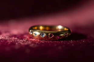 Close-up of minimalist gold wedding band on dark velvet with ruby and aquamarine accent stones