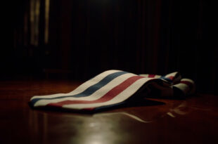 Red white and blue striped silk necktie on dark wooden surface under dramatic lighting