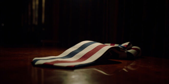 Red white and blue striped silk necktie on dark wooden surface under dramatic lighting