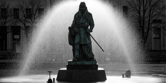 Bronze statue on stone base in city square being cleaned by high-pressure water equipment