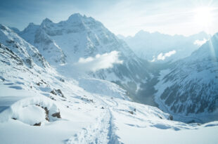 Snow-covered alpine mountain pass with thick white powder on peaks and valleys under overcast sky