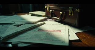 Stamped document papers and closed briefcase on polished wooden desk with red accent marks in dramatic lighting