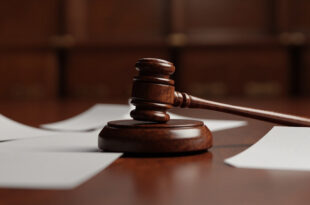 Wooden gavel resting on court bench with legal documents scattered nearby in empty courtroom.