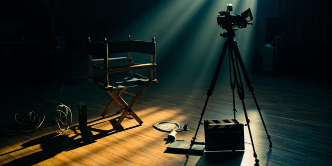 Film camera and directors chair on dark soundstage with dramatic lighting and production equipment scattered around