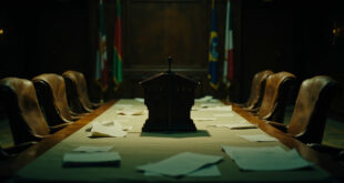 Empty diplomatic conference room with formal table, microphones, and international flags in background