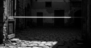 Weathered wooden door ajar, empty cobblestone courtyard, forensic tape across entrance, abandoned rural house exterior