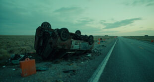 Overturned car on rural highway with debris scattered across asphalt under overcast sky