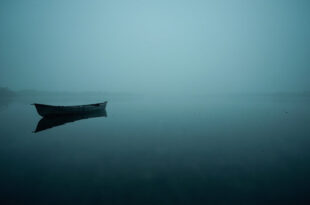 Empty fishing kayak floating on misty lake water during early morning hours