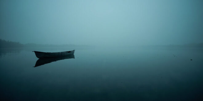 Empty fishing kayak floating on misty lake water during early morning hours