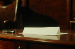 A folded white note with black pen resting on dark wooden desk surface in formal office setting