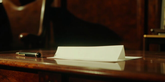 A folded white note with black pen resting on dark wooden desk surface in formal office setting