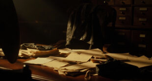 Vintage aviation documents and leather flight gear arranged on wooden desk in shadowy archive room