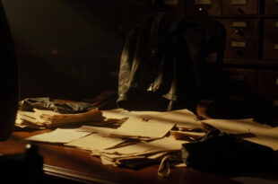 Vintage aviation documents and leather flight gear arranged on wooden desk in shadowy archive room