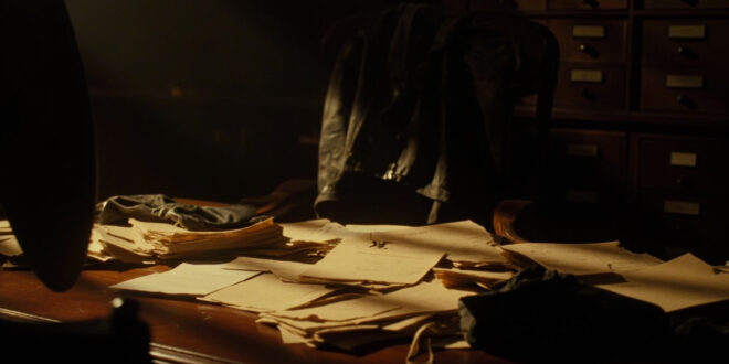 Vintage aviation documents and leather flight gear arranged on wooden desk in shadowy archive room