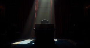 Empty leather chair behind wooden desk in formal chamber with burgundy curtains and dim lighting