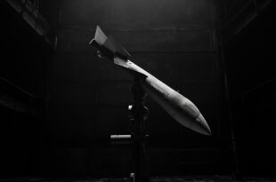 Tomahawk cruise missile on launch rail in dimly lit military storage facility with concrete and metal structures.
