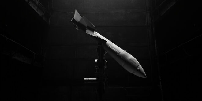 Tomahawk cruise missile on launch rail in dimly lit military storage facility with concrete and metal structures.