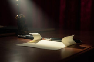 Cream paper note rests on polished wooden desk beside fountain pen in dramatic spotlight