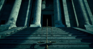 Imposing federal courthouse with tilted scales of justice casting long shadows on marble steps