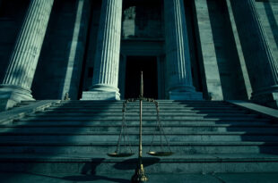 Imposing federal courthouse with tilted scales of justice casting long shadows on marble steps