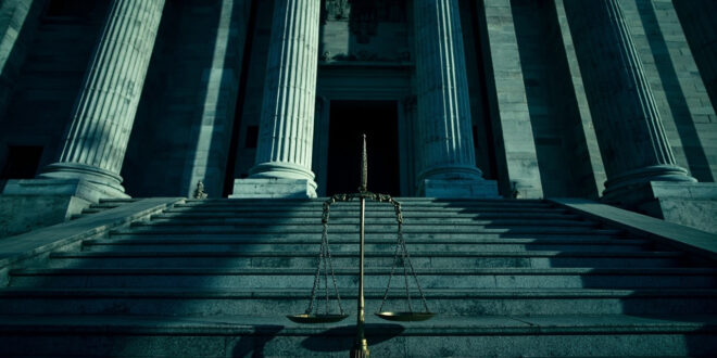 Imposing federal courthouse with tilted scales of justice casting long shadows on marble steps