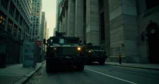 Military transport vehicles parked outside federal government building with concrete barriers and security perimeter.