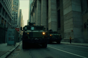 Military transport vehicles parked outside federal government building with concrete barriers and security perimeter.