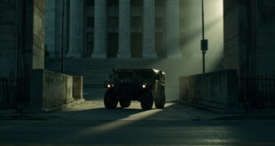 Military vehicle stationed outside concrete government building with security barriers on empty urban street