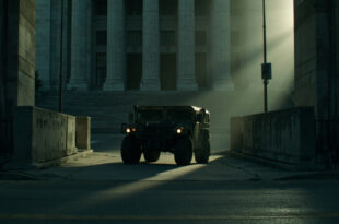 Military vehicle stationed outside concrete government building with security barriers on empty urban street