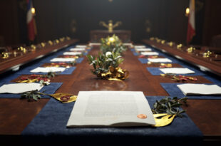 Formal diplomatic documents with seals and ribbons on polished wood table surrounded by international flags