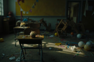 Empty classroom with scattered birthday decorations on wooden desk and overturned chairs