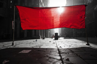 Red protest banner stretched across empty urban plaza with modern buildings under overcast sky